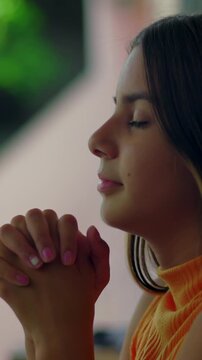 Serene young girl with clasped hands in prayer against wall outdoors, feeling faith