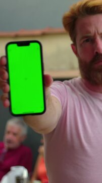 Serious man holding smartphone green screen at arm's length outdoors, display mockup