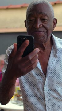 Smiling African American elderly man looking at smartphone outdoors, engaging with tech