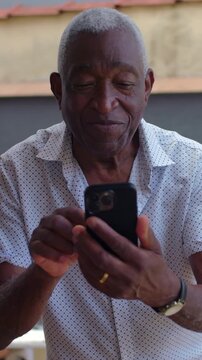 Thoughtful African American elderly man using smartphone outdoors at social event