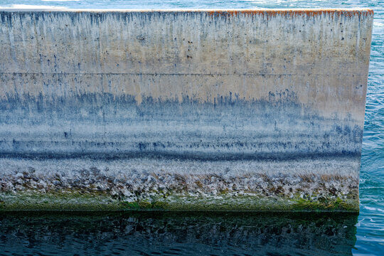 Abstract patterns of staining and aquatic growth on the concrete wall of a dam spillway