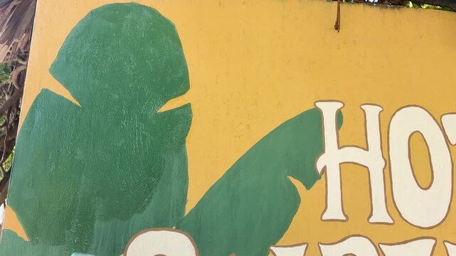 Close up of a green tropical leaf mural painted on a yellow wall with white lettering