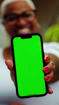 Woman presenting smartphone with green screen to camera, mobile mockup close up