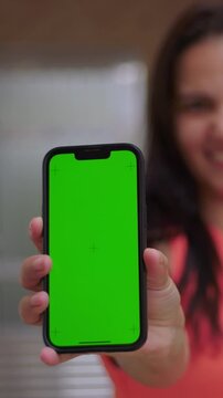 Woman showing vertical smartphone green screen to camera, mobile app mockup