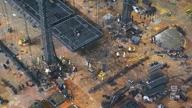 Cranes and construction crews assemble concert infrastructure inside a stadium lined with empty red seats.