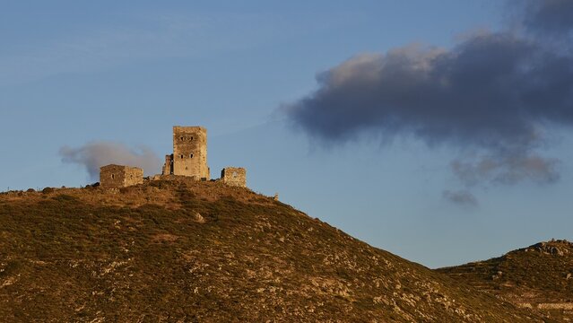 An old castle ruin perched on a grassy hill under a dramatic sky in the evening light, residential tower on a mountain, Mani Peninsula, Peloponnese, Greece