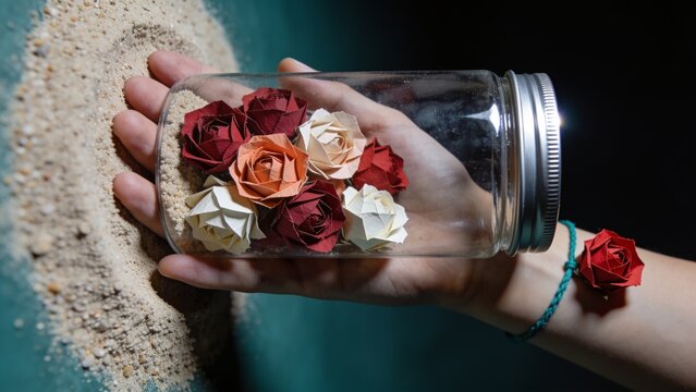 Hand holding glass jar filled with small red roses on sand background