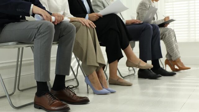 Group of people waiting in queue for job interview on chairs indoors, closeup