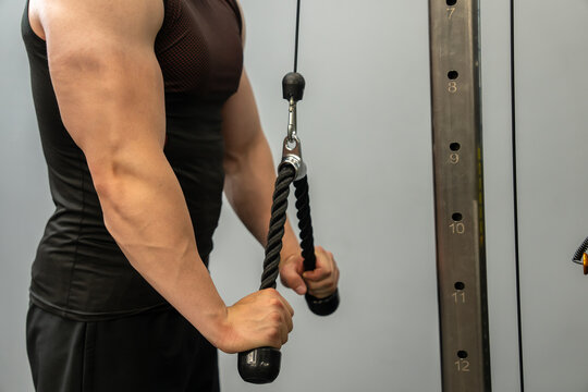 A muscular man performs a triceps rope exercise.