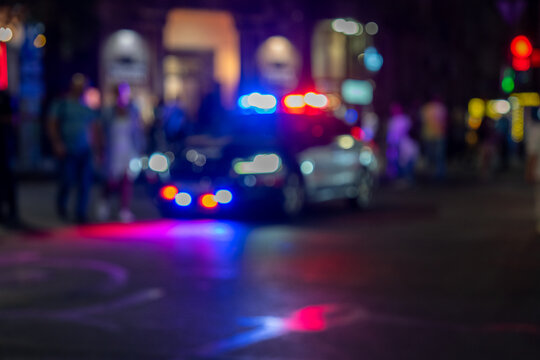 A nighttime city scene featuring a police car with its red and blue flashing lights on.