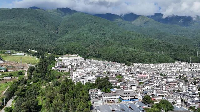 Aerial footage of a white-walled town below green mountains covered with clouds, Southwest China, D-Log lossless file format