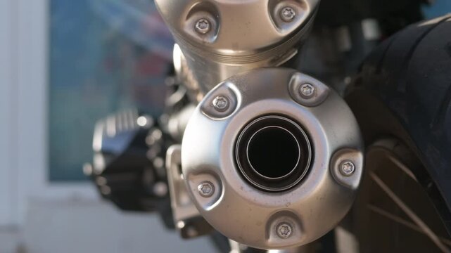 Close-up of round brushed steel exhaust end caps of a motorcycle with the rear tyre and a blurred shop window behind, French Riviera, France.