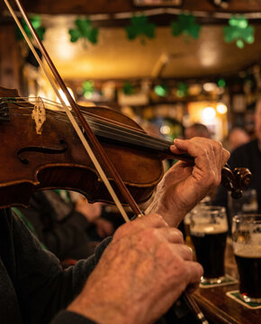 Older man playing violin in a pub with pints of beer around him  