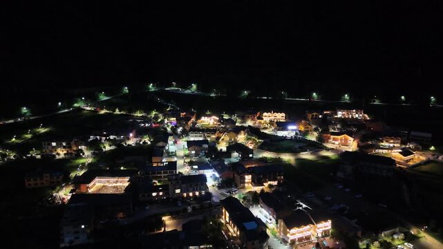Aerial night flyover of a mountain lakeside town with warm lights at Lugu Lake, Southwest China, D-Log lossless file format
