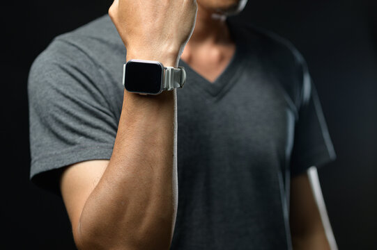 Close-up of a man wearing a smartwatch on his wrist, black and gray clothing, casual style, dark background, fitness health concept