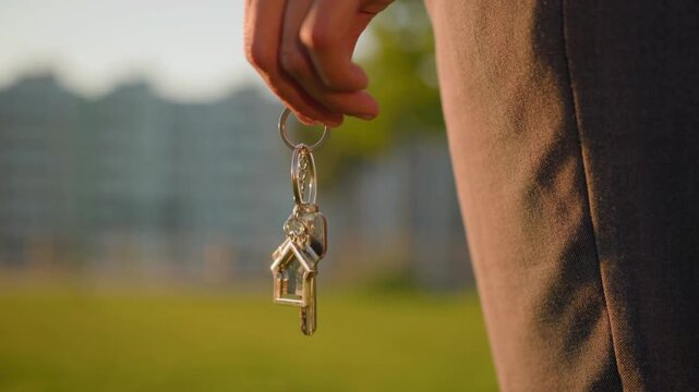 Close-Up of House Keys Against a Green Residential Background. Close-up of house keys held outdoors against a softly blurred residential background, representing homeownership, property purchase. 