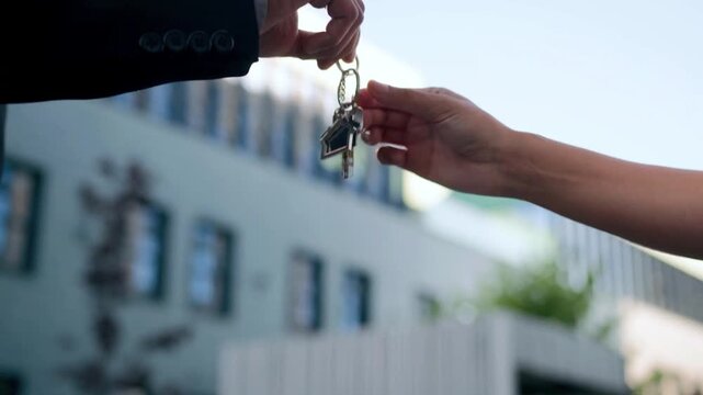 House Keys Being Handed Over During a Real Estate Property Transaction. Two people exchange house keys outside a residential building, representing property handover, successful home purchases. 
