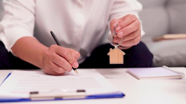 Close-Up of a House Key Against a Modern Residential Building. Close-up of a house key held against a softly blurred residential building, representing property ownership, real estate investment. 
