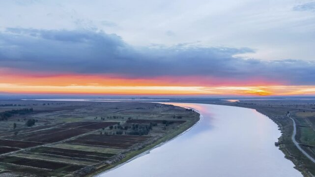 Aerial sunrise time-lapse over the Yellow River valley, golden light sweeping meandering water, sorghum fields and hills, Baotou city, Inner Mongolia, China.
