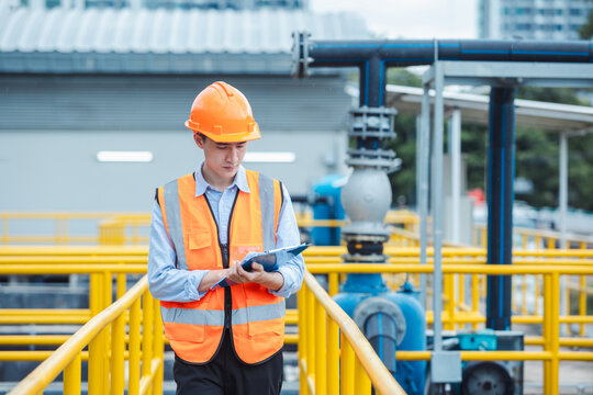 Young male engineer wearing vest and hard hat holding a clipboard inspecting wastewater in an industrial plant.
