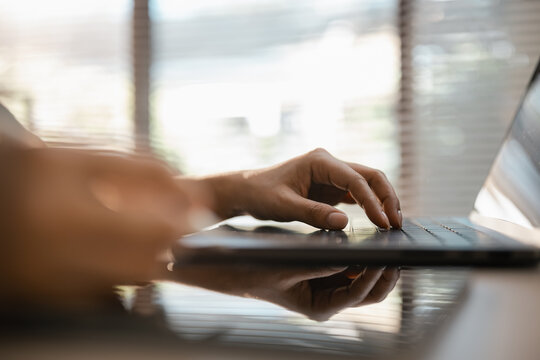 Hands typing on a laptop keyboard show computer work in a sunlit workspace. The laptop remains central to this digital task, with fingers framed by a cropped torso and soft background.