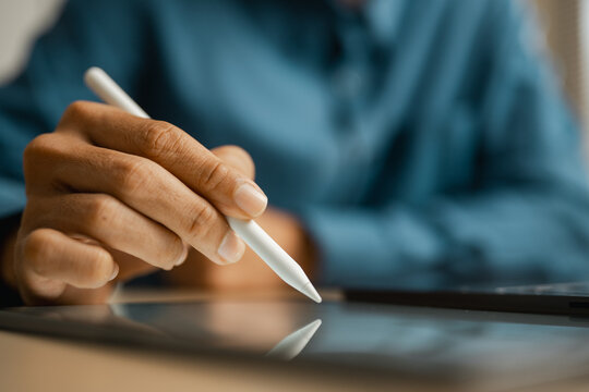 Hands using a stylus on a tablet show digital technology in a tight closeup. The stylus is held for precise screen input, with a cropped torso behind the softly illuminated work surface.