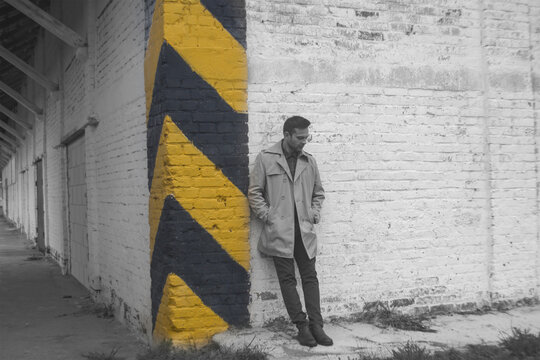 ad man in trench coat standing near yellow safety stripes wall with copy space