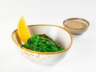 Yellow lemon wedge, green seaweed salad in ceramic bowl with dipping sauce, Asian bistro appetizer © Andrei Starostin
