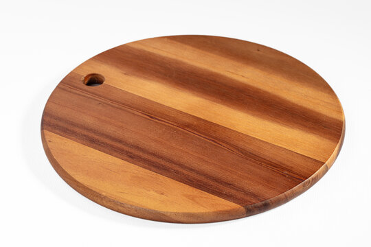 Round acacia wood serving board with hanging hole on white background, empty rustic platter for kitchen and food styling
