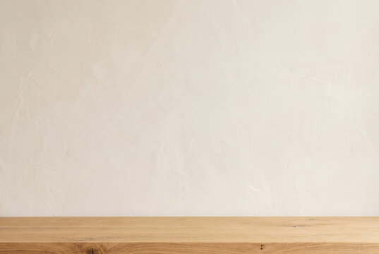 Empty oak tabletop in front of textured cream plaster wall
