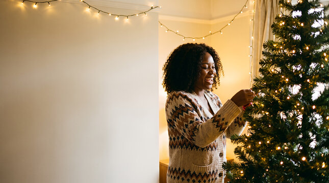 Woman decorating Christmas tree with joy indoors