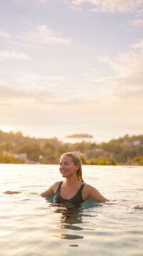 Woman in calm water gazing away during golden sunset light