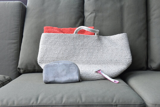 Woven tote bag with coral towel and grooming essentials on a grey outdoor sofa