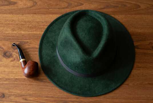 Quiet study of a dark green felt hat and curved tobacco pipe on warm wood