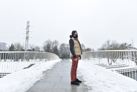 Bearded man in puffer vest standing on snowy bridge
