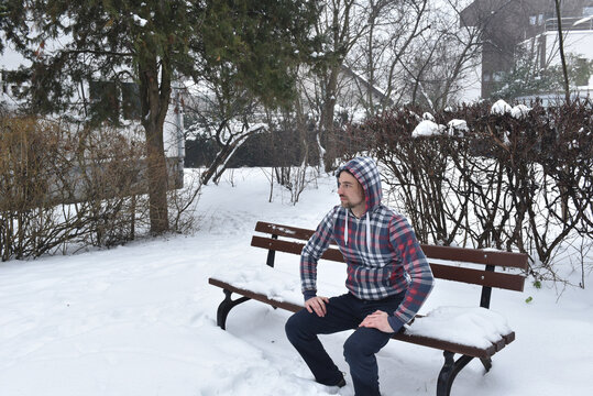 Man in plaid hoodie sitting on snowy park bench
