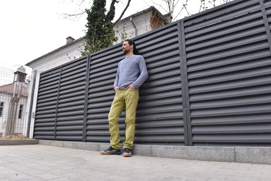 Low angle view of a man in casual attire standing against a modern anthracite louvered fence
