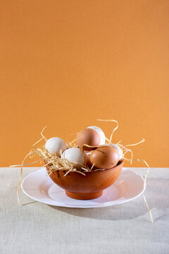 Fresh chicken eggs in a bowl with wood shavings on a colored background.