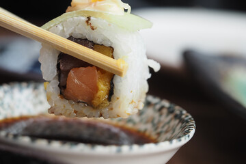 Chopsticks hold a sushi roll above a serving dish during a meal © Towfiqu Barbhuiya 