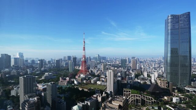 Feathery cirrus clouds streaming across a bright blue sky above the Tokyo cityscape in timelapse, a red and white steel tower and a modern glass skyscraper standing over the city