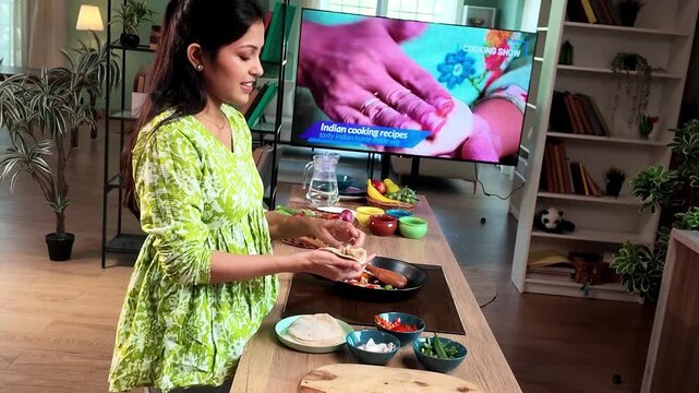 Young Indian woman learning to prepare traditional modak dumplings in a modern kitchen while watching a cooking recipe on TV, Indian cuisine, homemade food and culinary skills concept.