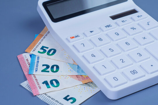 White desk calculator on euro banknotes including 50, 20, 10 and 5 euro bills. Financial calculation, budgeting, taxation, cost and business accounting concept.