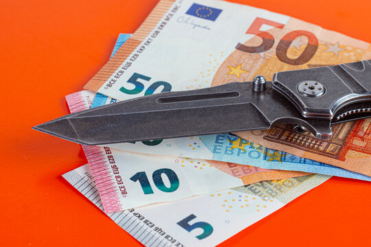 Folding knife on euro banknotes against orange background. Finance, budget cutting, cost reduction and economic crisis concept.