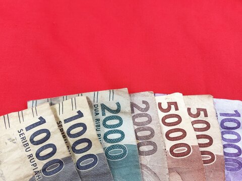 Indonesian Rupiah paper banknotes arranged in ascending order of denomination: 1,000, 2,000, and 5,000, 10,000 Rupiah isolated on red background