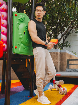 Thoughtful young Asian man in casual athletic wear leaning on a colorful playground structure.