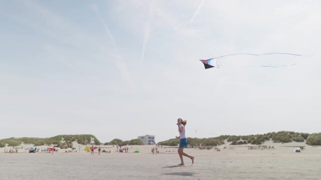 Girl running barefoot with a kite on a sandy beach sand dunes with grass in the background