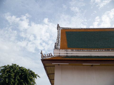 Traditional Thai Temple Roof with Green and Orange Tiles Against a Cloudy Blue Sky