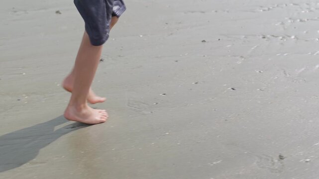 The boy's feet are walking on wet sand unrecognizable child on the seashore