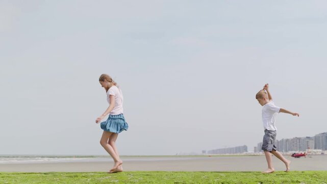 Girl and boy walking barefoot with kites on green algae shore slow motion side view tilt camera movement