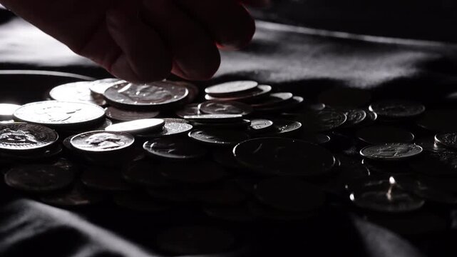 Personal finance, hand taking coins from pile of silver money on dark table